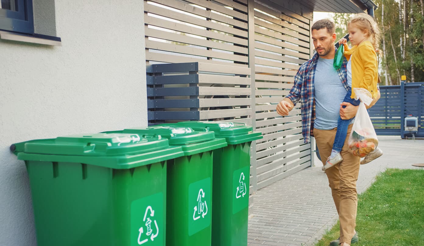 Parent teaches child proper waste sorting at recycling bins.