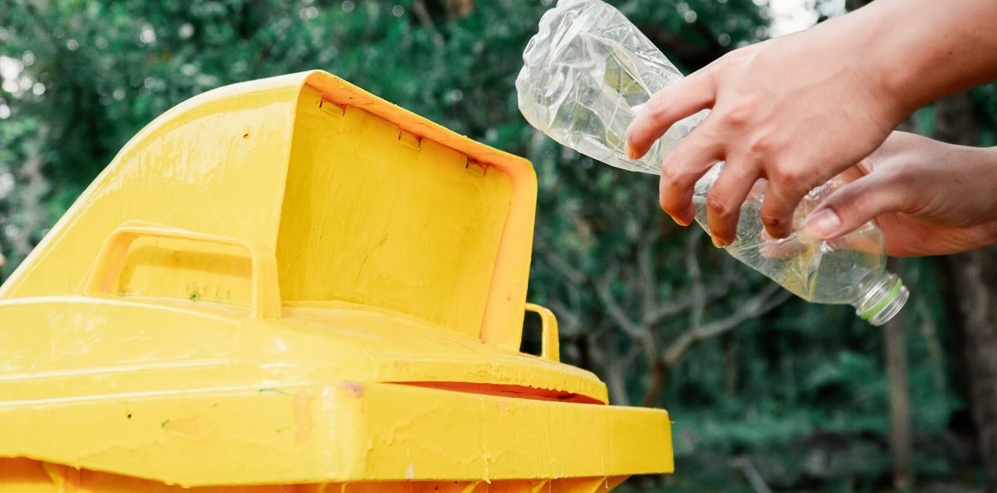Personne jetant un bouteille plastique dans un bac jaune de recyclage