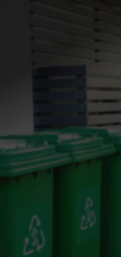 Person throws a plastic bottle into a bright yellow recycling bin.