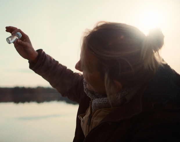 Person holding water sample against sunlight, highlighting plastic pollution crisis.