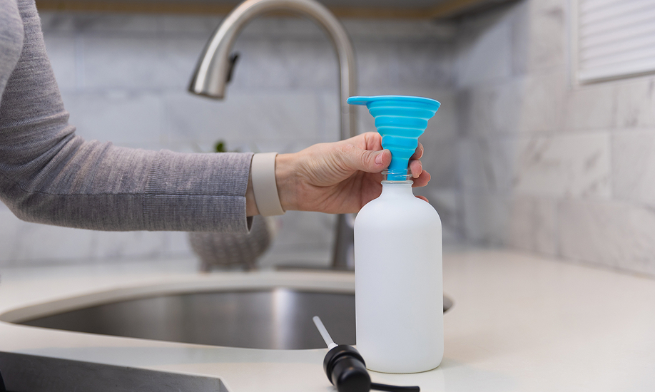 A hand next to a sink holds a blue funnel in a soap bottle.