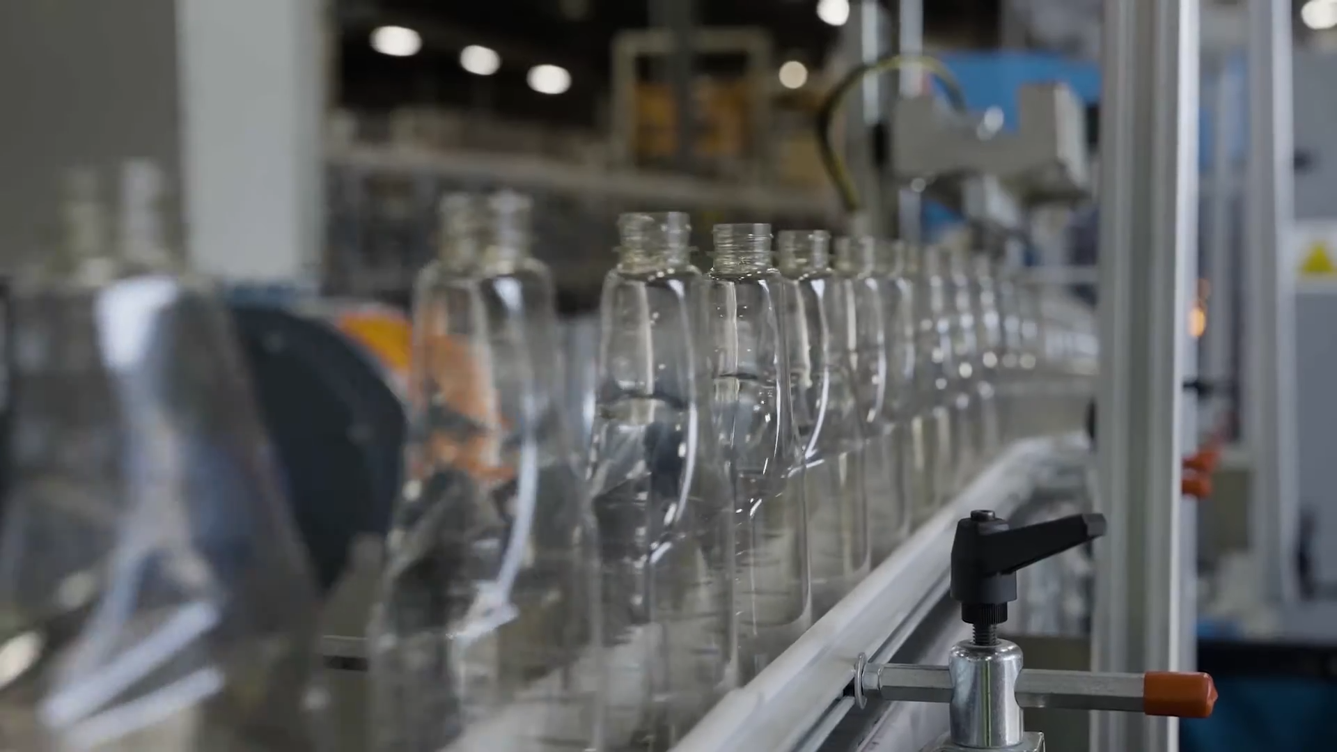 A long row of empty, clear plastic bottles moving along a factory conveyor belt.